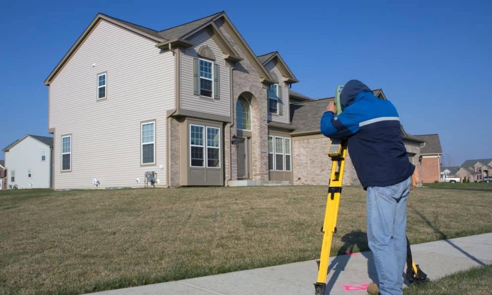 Land surveyor using equipment for a boundary survey outside a residential home to define property lines and prevent legal issues
