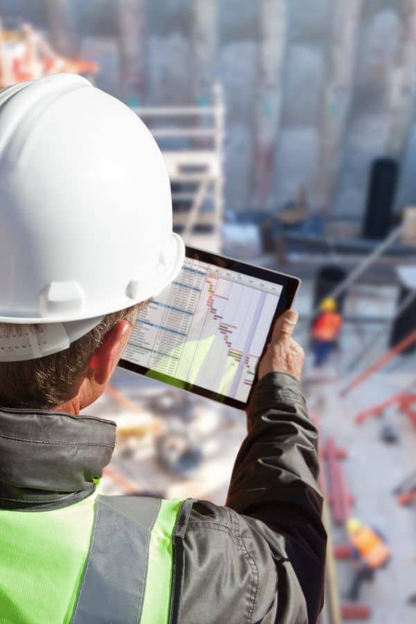 Construction management professional in safety gear using a tablet to track resources and schedules at a Denver construction site
