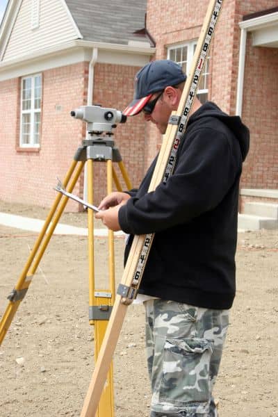 Surveyor measuring a residential property in Denver to complete a FEMA elevation certificate for insurance purposes

