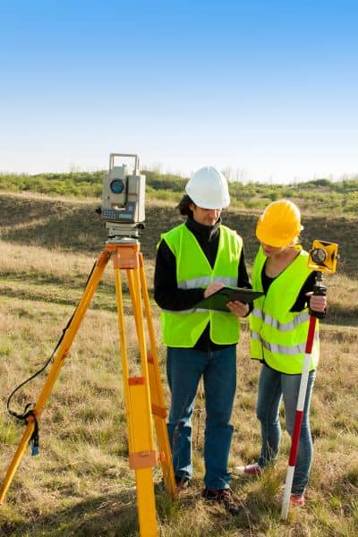 Construction management team in Denver reviewing land survey data on-site with total station and elevation rod
