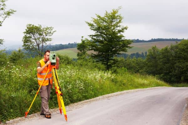 Land surveyor collecting elevation data on a sloped site for a topographic survey near a road in Denver
