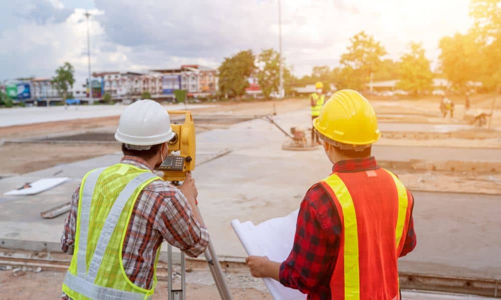  Construction survey being performed by two surveyors with total station and plans on a roadway site
