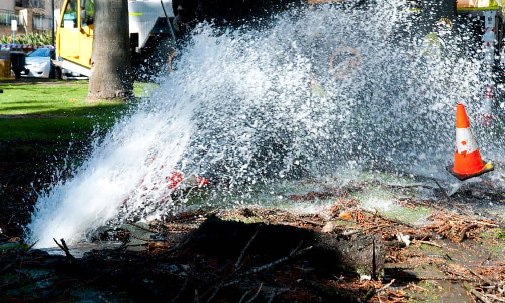 Water spraying from a burst underground pipe during a water-main break, highlighting the need for an emergency-ready due diligence survey