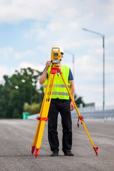 A surveyor performing a topo survey on a roadway using a total station to measure elevations for upcoming infrastructure improvements