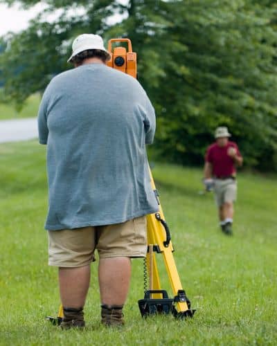 A professional land surveyor using field equipment to mark accurate boundaries, showing how a real boundary line survey is done