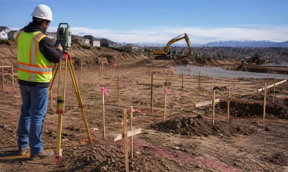 Land surveyor using a total station to mark construction staking points on an active job site before foundation and site development work begins